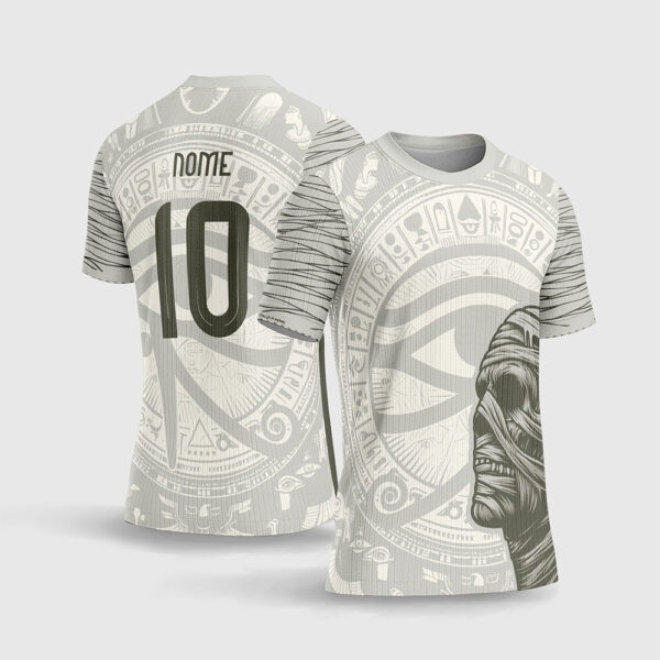 Arte Vetor Camisa de Interclasse Múmia Egito.jpg apresenta o mockup de uma camisa de interclasse na cor bege creme com ilustração em perfil de uma múmia detalhada, grande mandala com o Olho de Hórus, hieróglifos concêntricos e numeração moderna em sublimação total CorelDRAW.